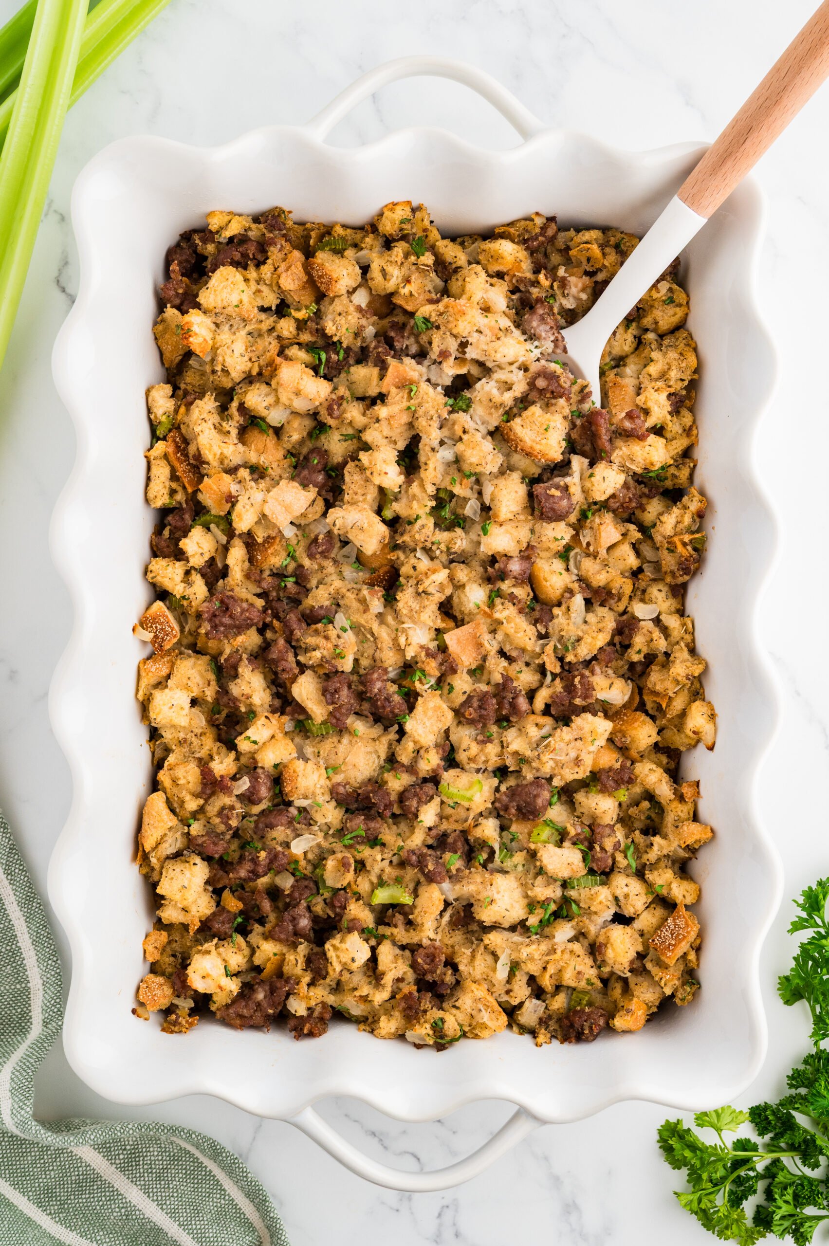 Serving spoon lifting a scoop of baked sage and sausage stuffing with golden edges.