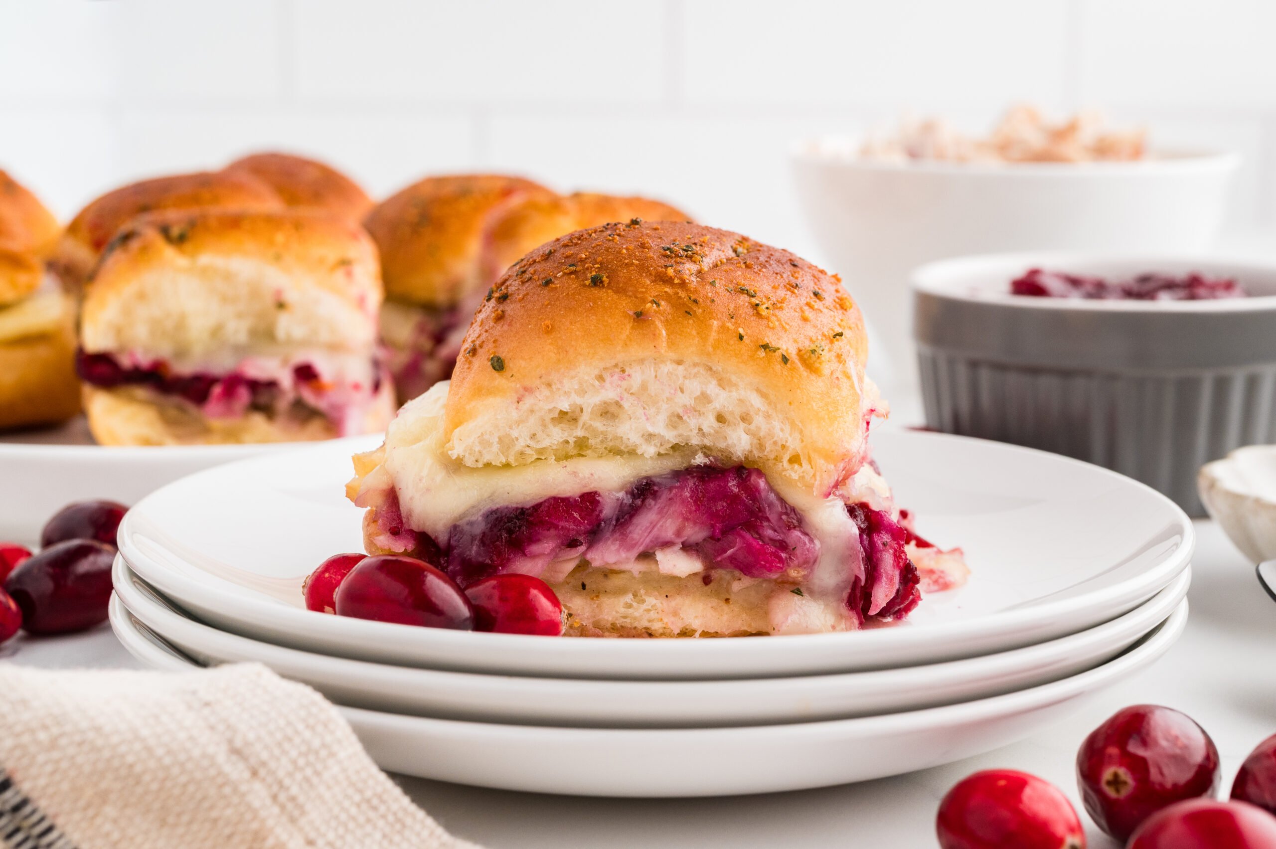 Cranberry turkey slider on a white plate with visible layers of turkey, cranberry sauce, and melted cheese.