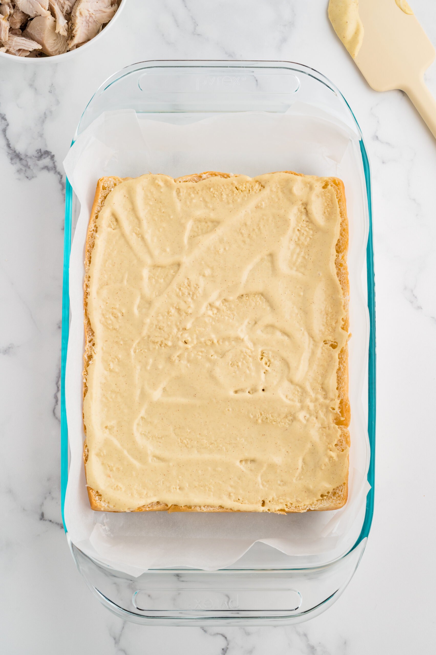 Dinner rolls that have been sliced in half in a clear baking dish with dressing spread over the bread.