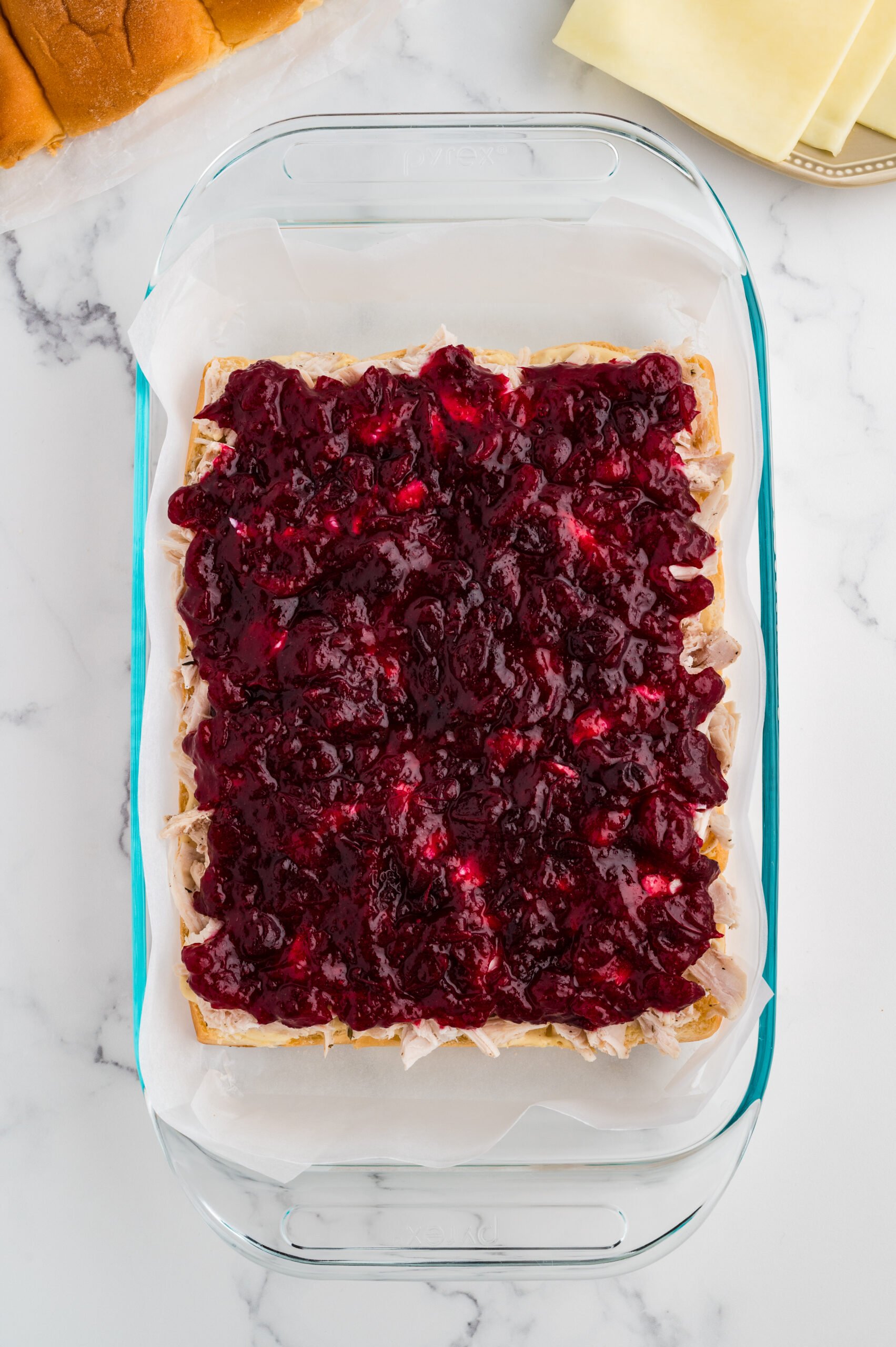 Shredded turkey topped with a thick, even layer of cranberry sauce in a baking dish.