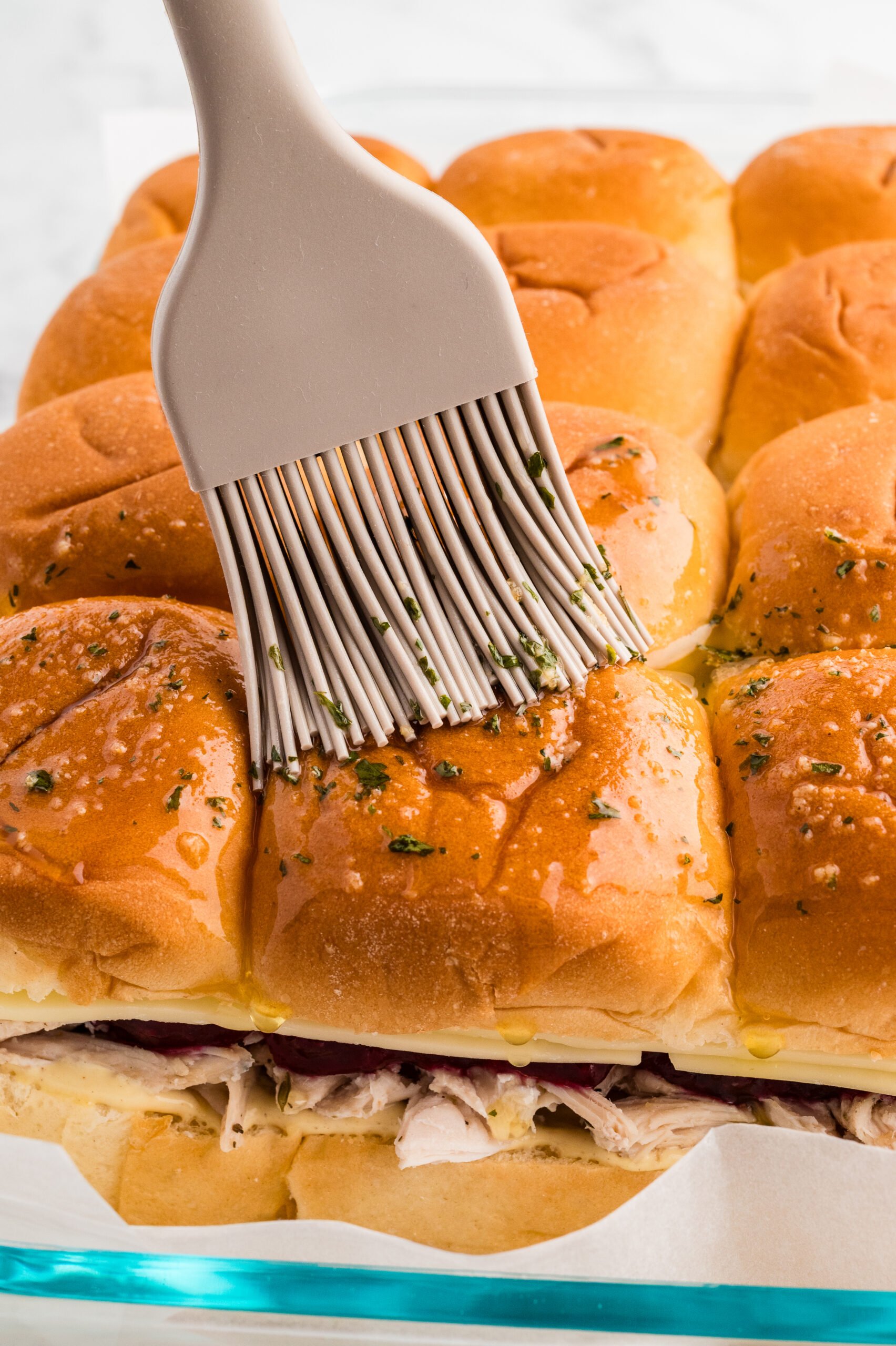 Close up of a pastry brush spreading garlic butter over the tops of the slider rolls.