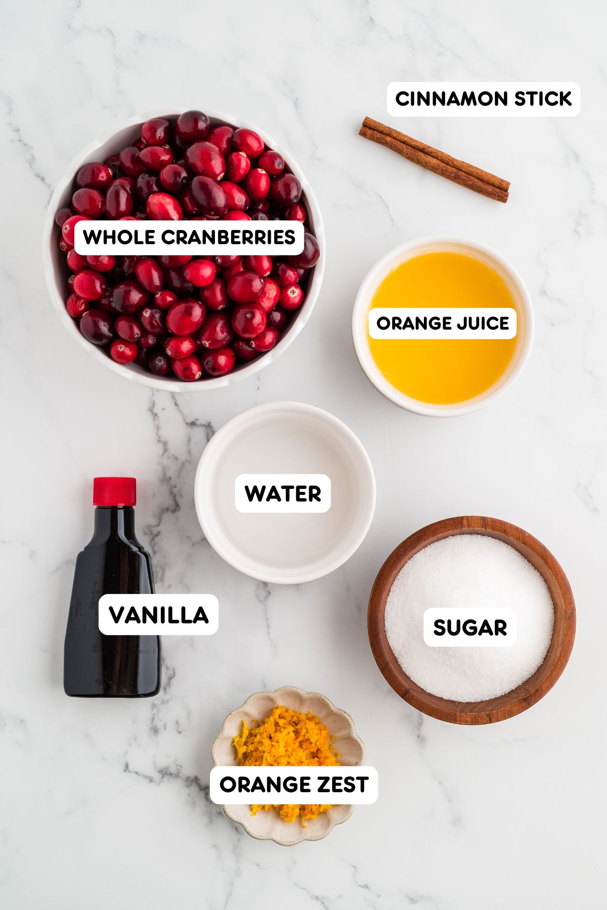 Bowls of fresh cranberries, orange juice, water, sugar, orange zest, vanilla, and cinnamon stick for whole berry cranberry sauce on a marble counter.