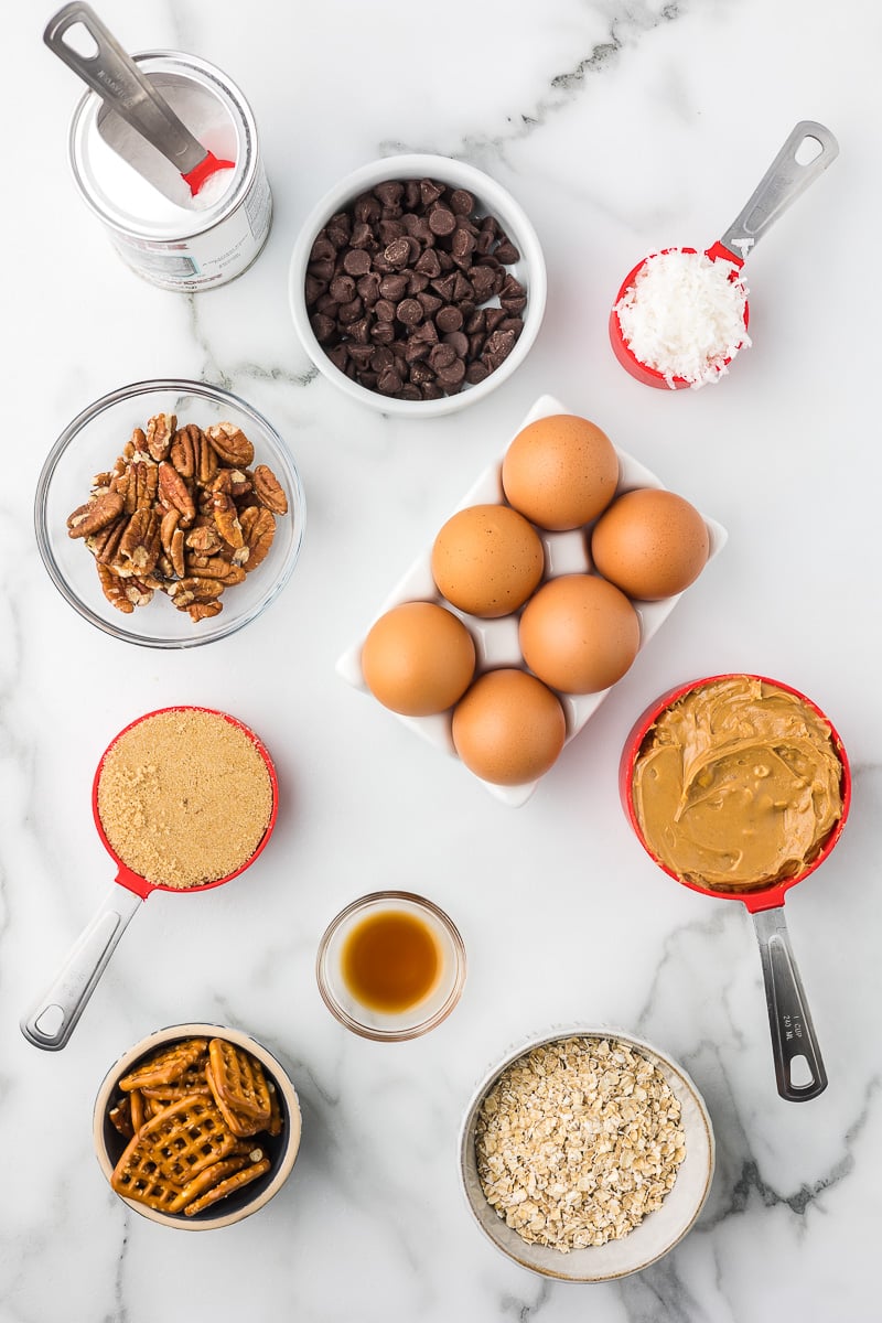 Ingredients for peanut butter breakfast cookies including oats, peanut butter, eggs, chocolate chips, pecans, coconut, pretzels, brown sugar, and vanilla.
