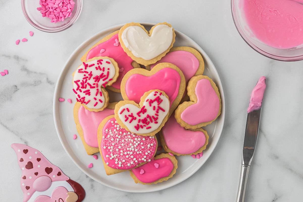 Cut-out sugar cookies on a white plate that have been decorated for Valentine's day. 