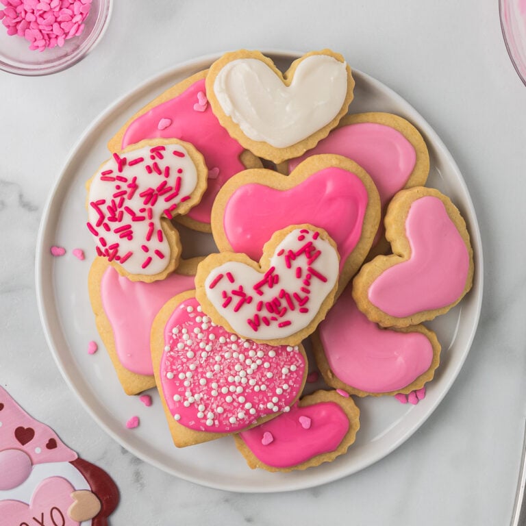 Decorated cut-out sugar cookies on a white plate stacked on one another.