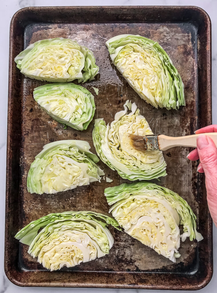 Brushing olive oil onto thick cabbage steaks before roasting in the oven.