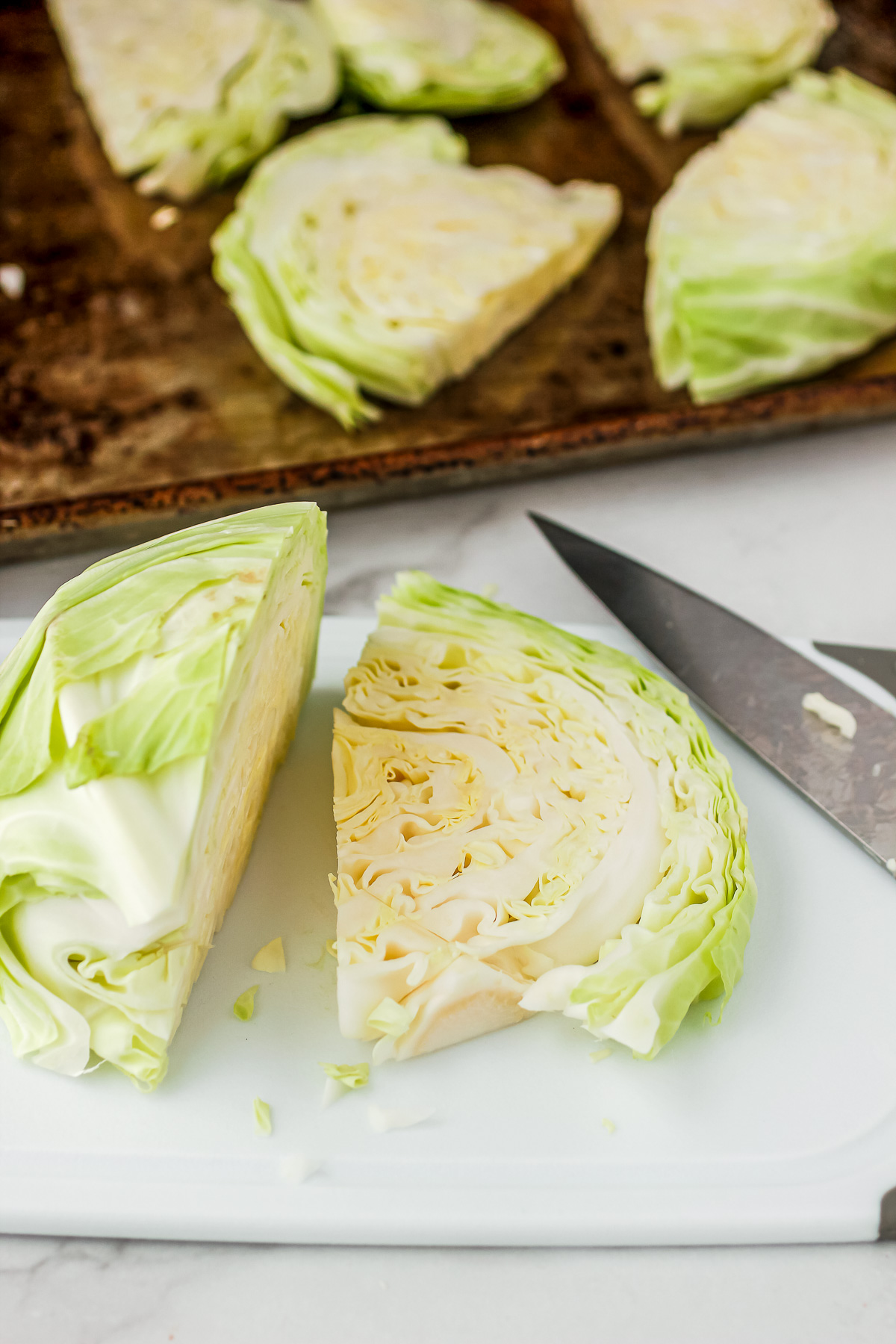 Thick ½ inch cabbage steaks cut on a white cutting board before roasting.