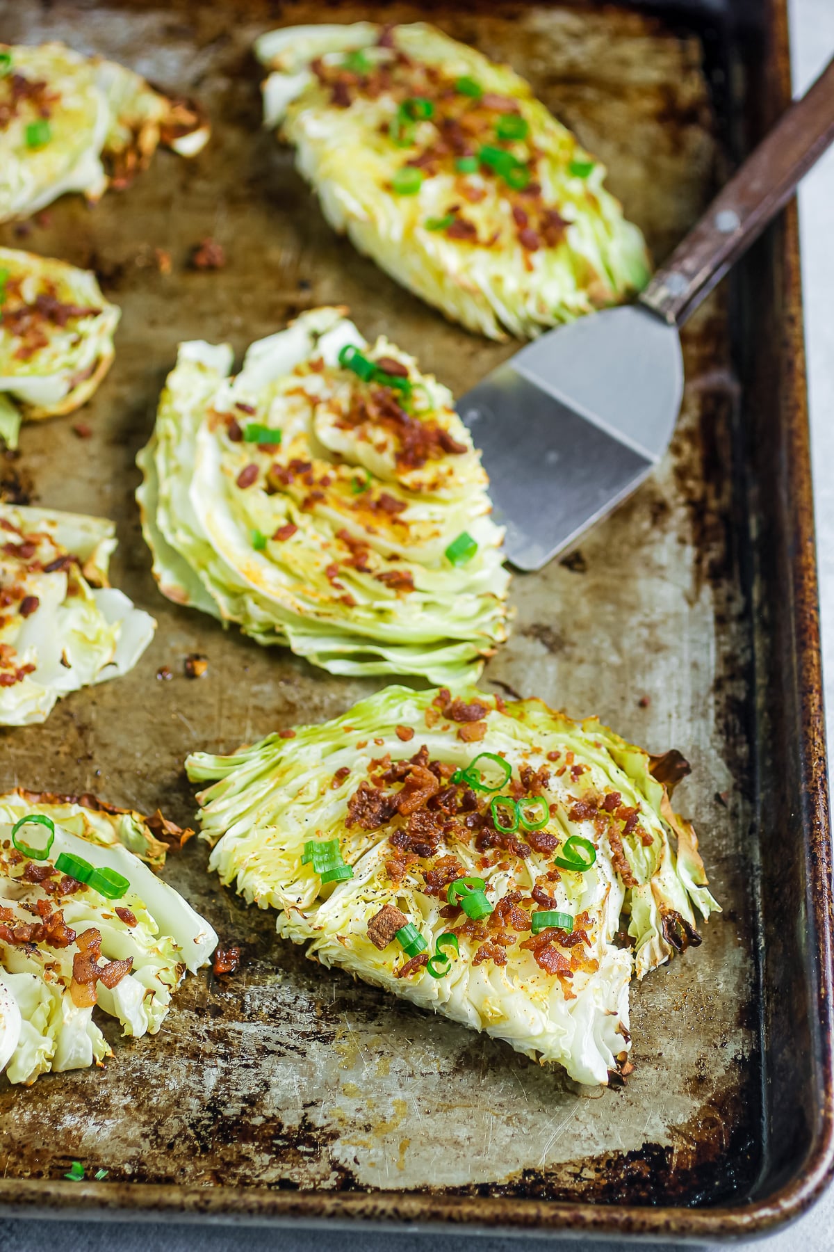 Roasted cabbage steaks with crispy bacon and green onions on a sheet pan.