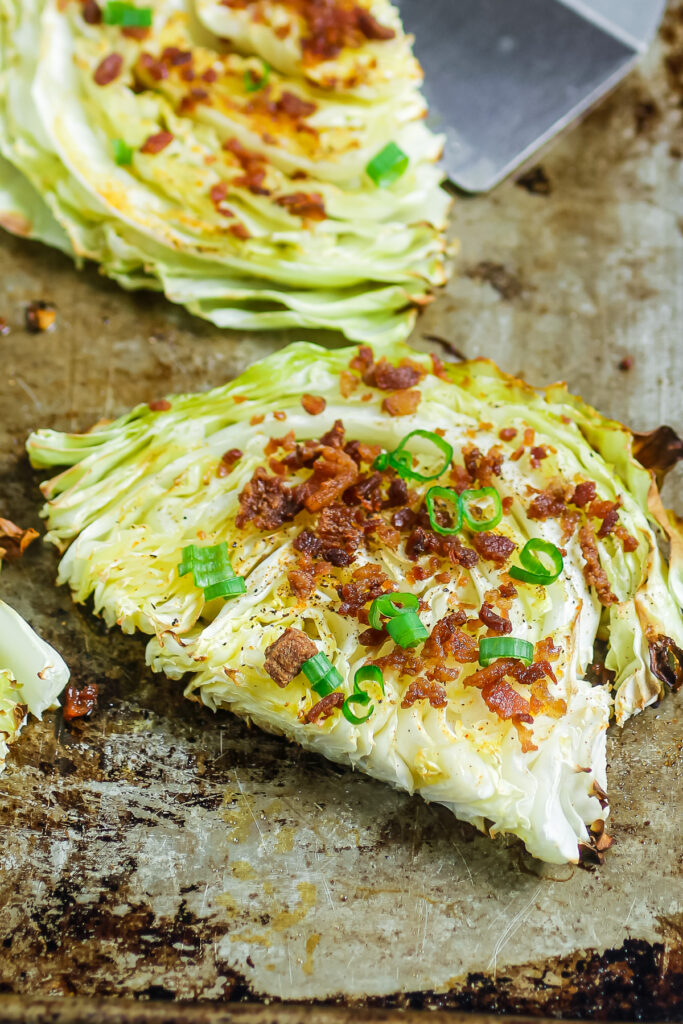 Roasted cabbage steaks just out of the oven with crispy bacon and green onions on a sheet pan.