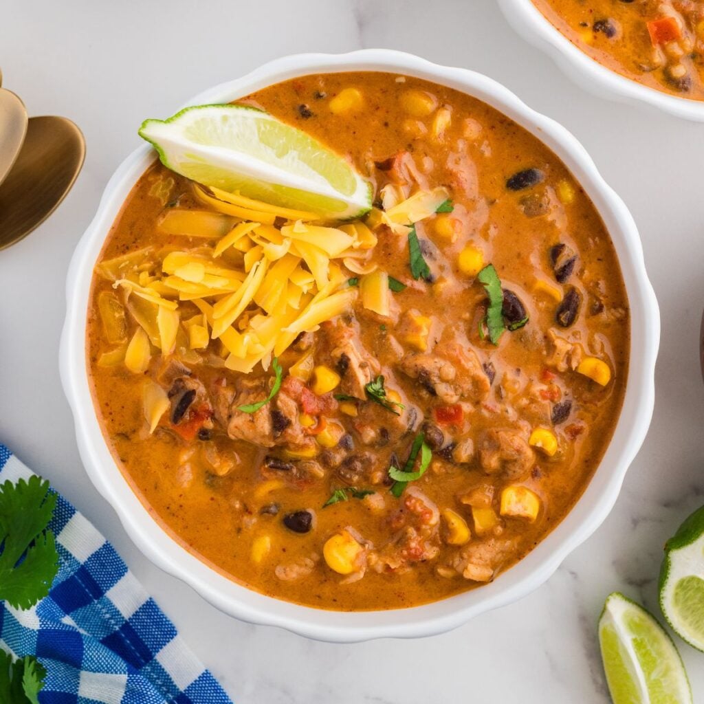 Creamy chicken taco soup with black beans, corn, rice, and shredded cheese topped with a lime wedge.