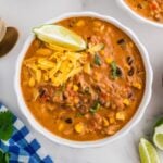 Creamy chicken taco soup with black beans, corn, rice, and shredded cheese topped with a lime wedge.