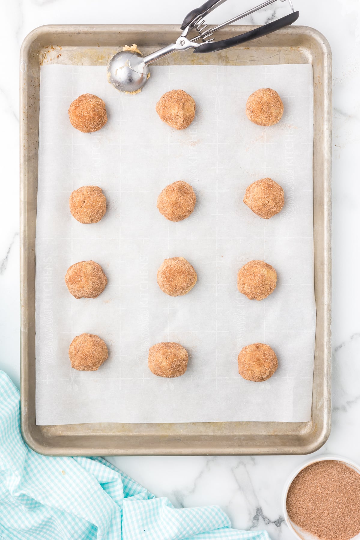 Cinnamon sugar cookie dough balls on a parchment-lined baking sheet before baking.