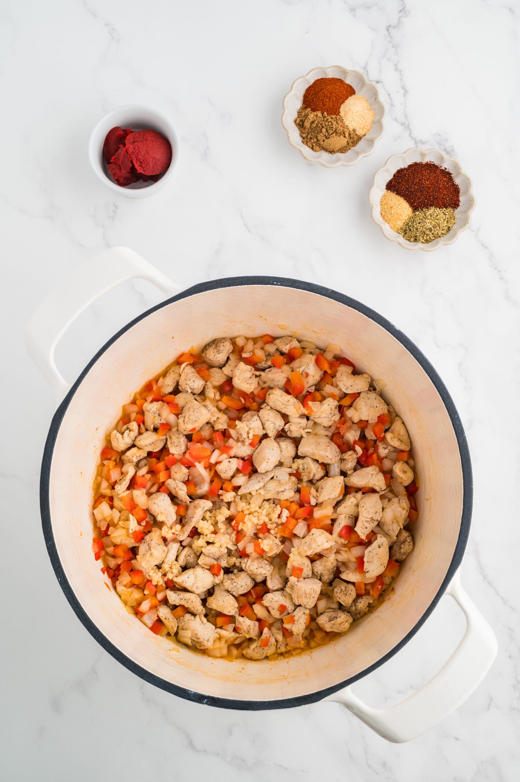 Cooked chicken with onion and red bell pepper in a pot for taco chicken soup.