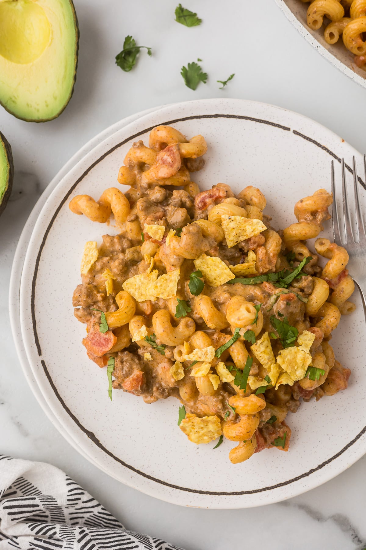 Mexican mac and cheese with ground beef topped with tortilla chips and cilantro on a plate.