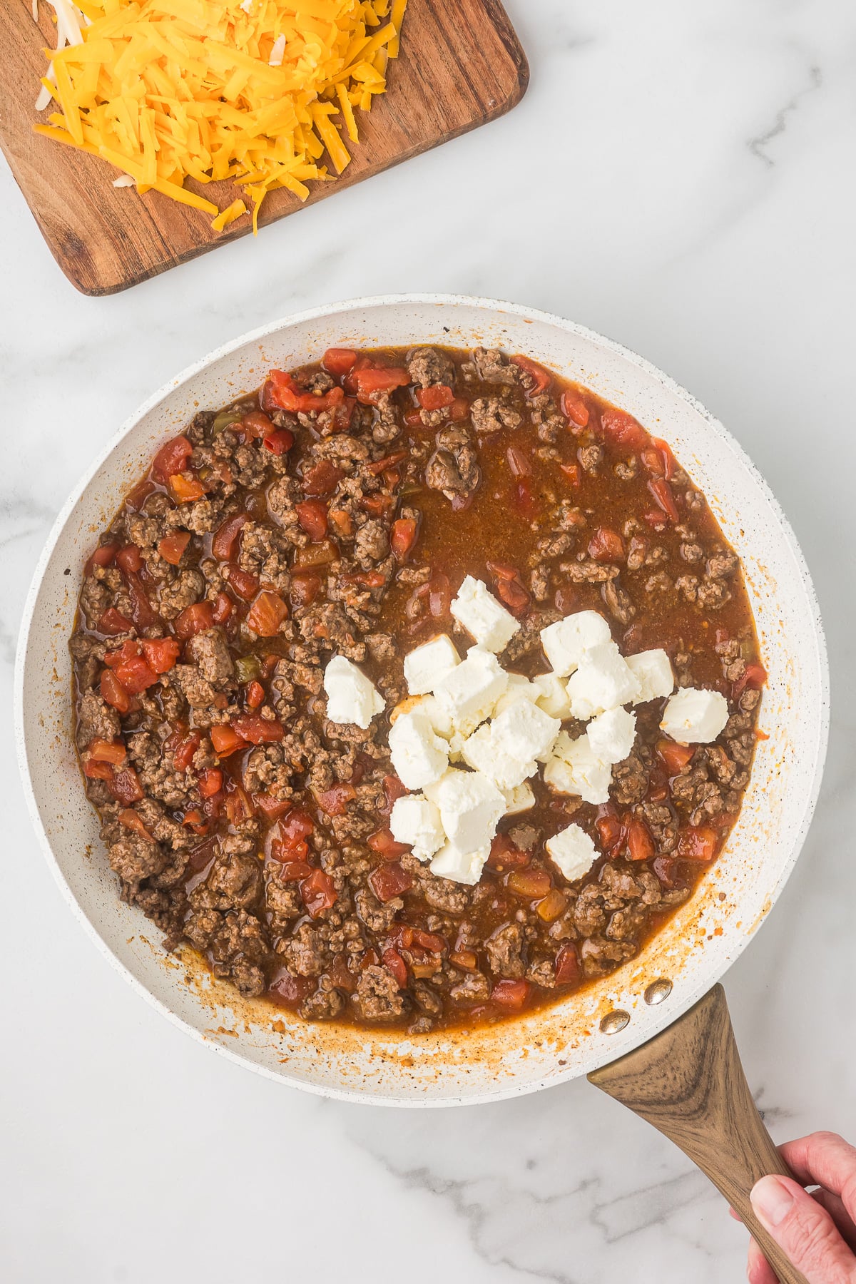 Cream cheese melting into enchilada beef mixture to create a creamy sauce for Mexican mac and cheese.