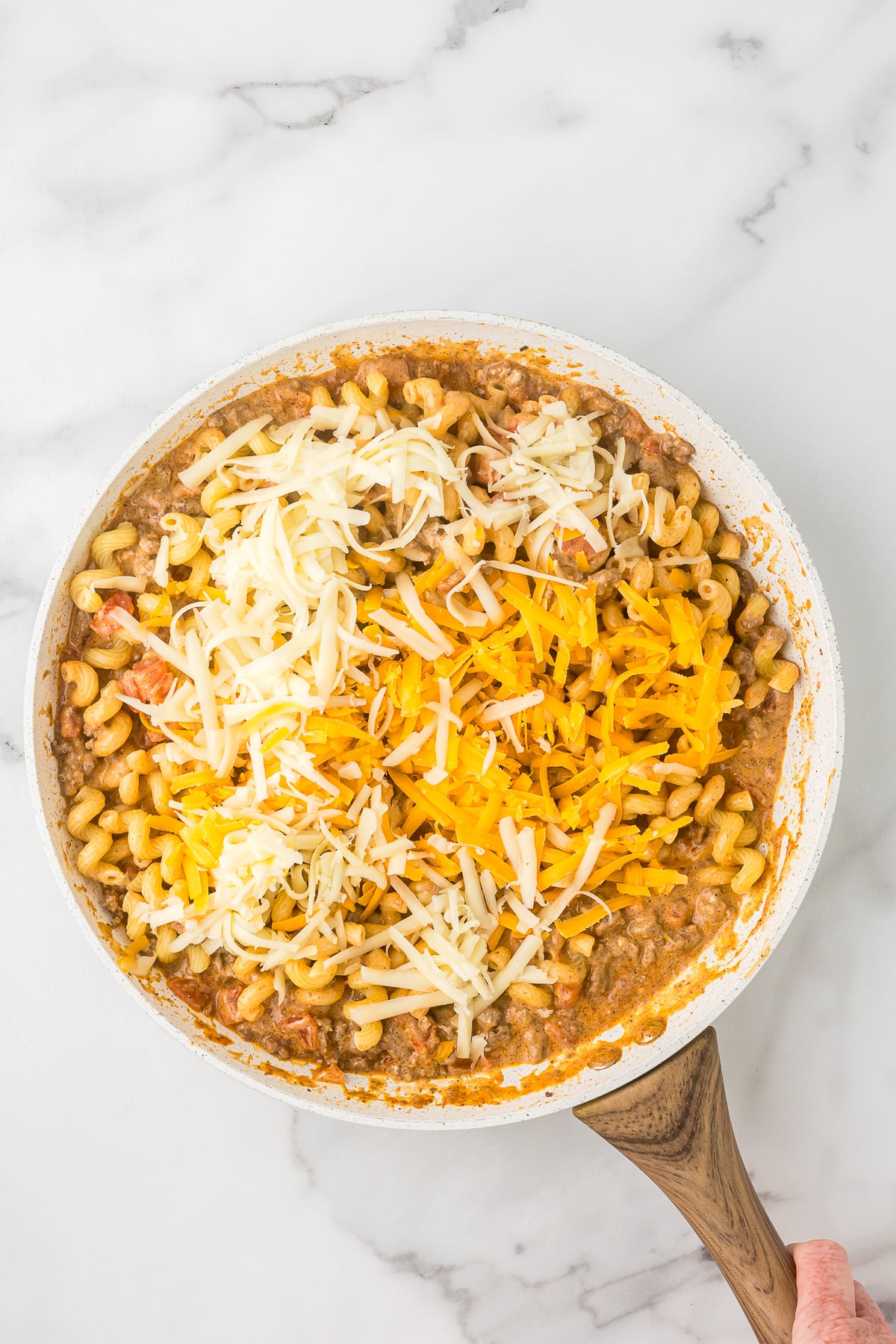 Shredded cheddar and Monterey Jack cheese melting into Mexican mac and cheese in skillet.