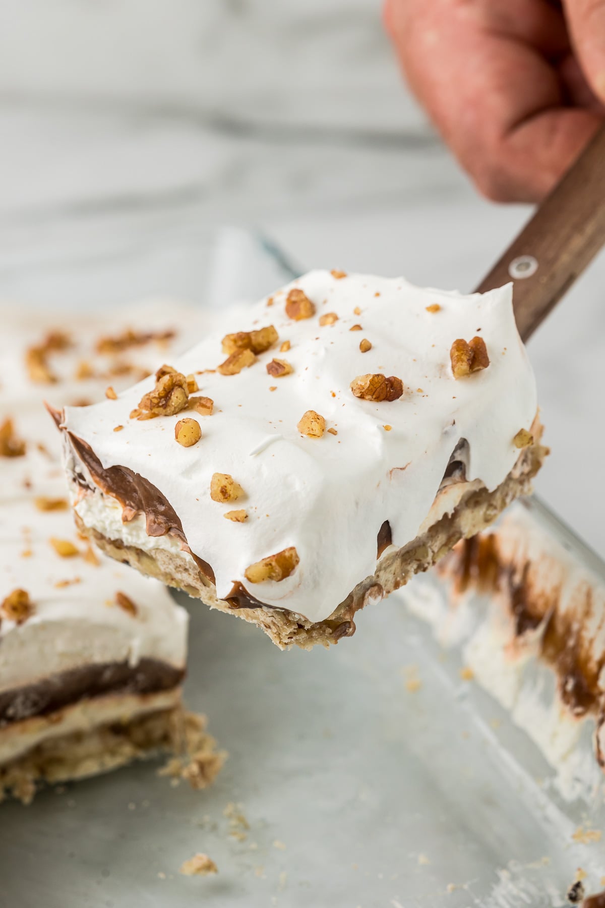 Layered Chocolate Delight lifted from the pan showing pecan crust, cream cheese filling, chocolate pudding, and whipped topping.