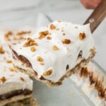 Layered Chocolate Delight lifted from the pan showing pecan crust, cream cheese filling, chocolate pudding, and whipped topping.