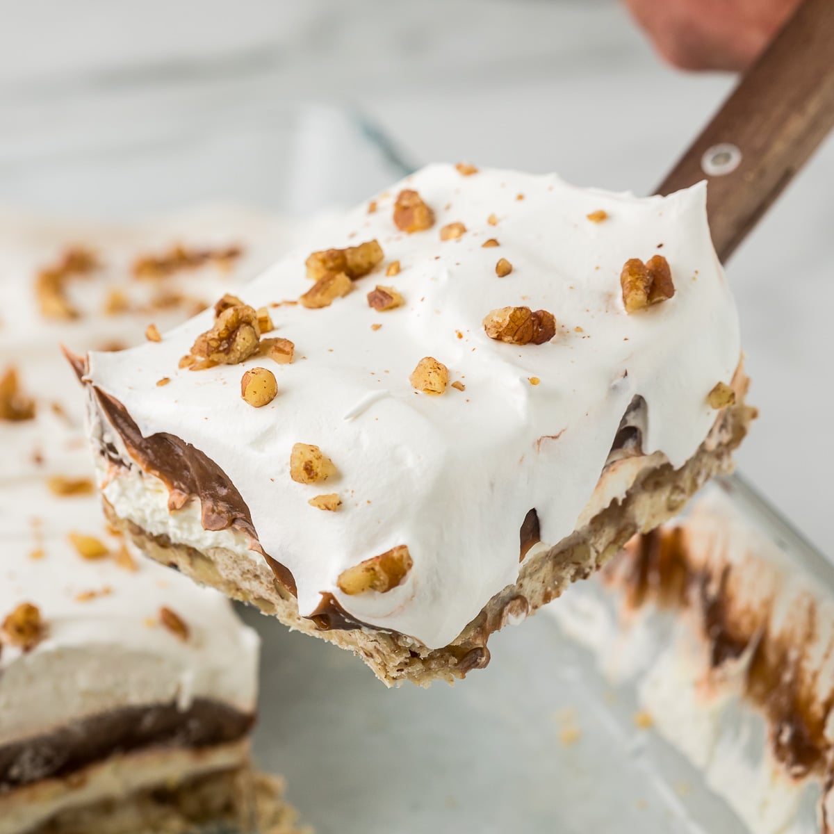Layered Chocolate Delight lifted from the pan showing pecan crust, cream cheese filling, chocolate pudding, and whipped topping.