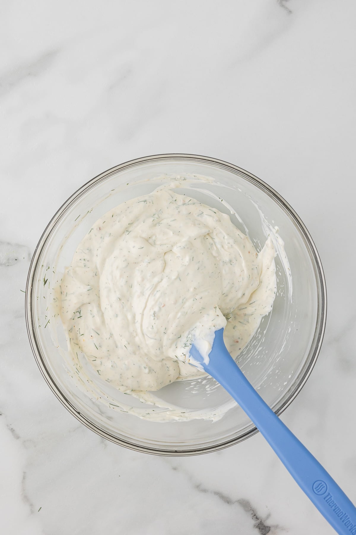 Dill dip in a mixing bowl with a blue spatula.