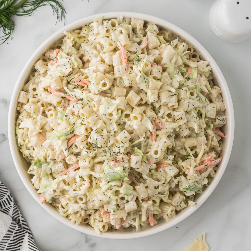 Creamy Coleslaw Pasta Salad in a white bowl with a napkin, salt and pepper shakers and some fresh dill.