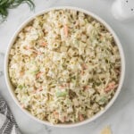Creamy Coleslaw Pasta Salad in a white bowl with a napkin, salt and pepper shakers and some fresh dill.
