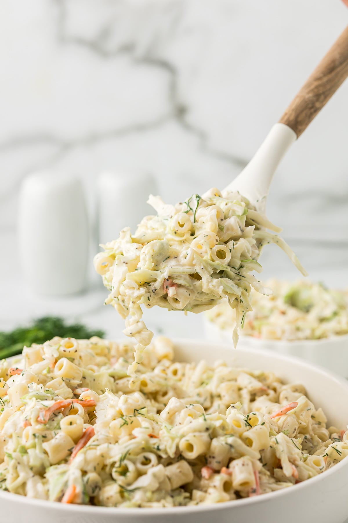Creamy Coleslaw Pasta Salad on a white spoon hovering over a bowl of the salad.