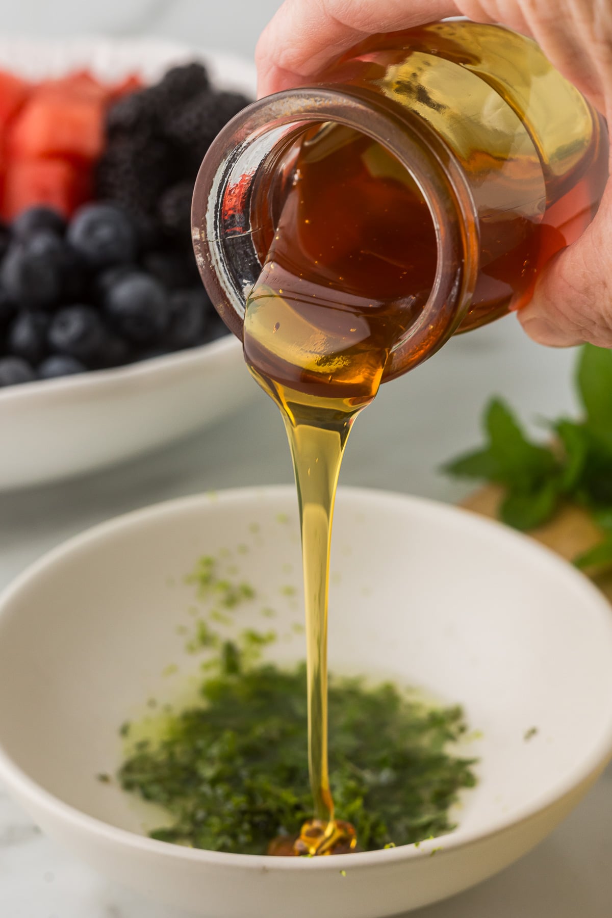 Honey being poured into a bowl with lime juice, zest, and mint for a simple fruit salad dressing.