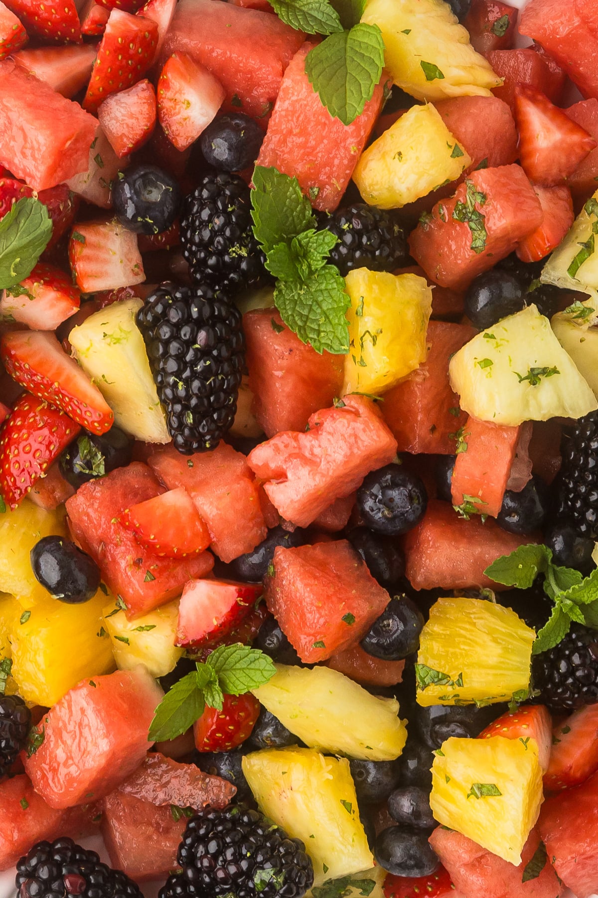 Close-up of summer fruit salad with watermelon, pineapple, blueberries, blackberries, strawberries, and fresh mint.