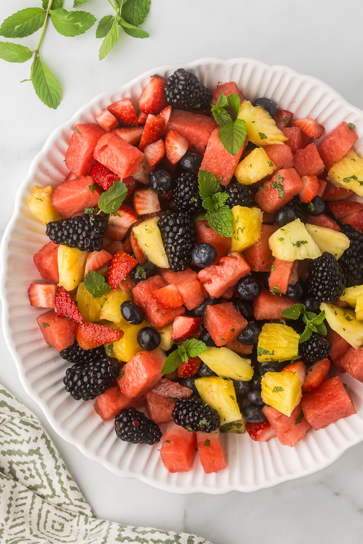 Fresh berry and watermelon fruit salad with pineapple and mint on a serving platter.