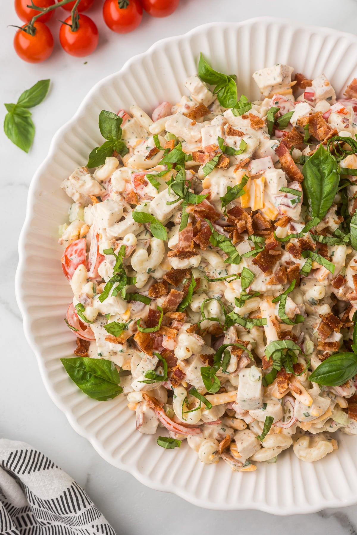 Creamy BLT Chicken Pasta Salad garnished with crispy bacon and fresh basil in a white serving bowl.
