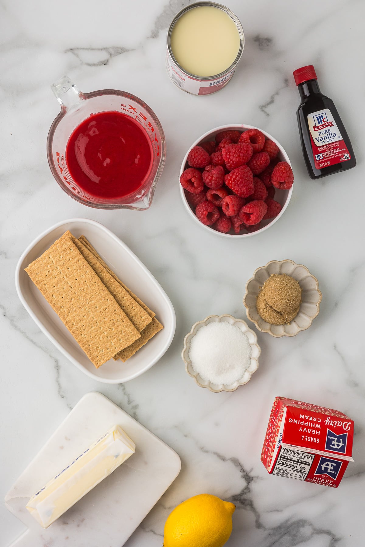 Ingredients for No-Bake Raspberry Lemonade Pie including graham crackers, raspberries, sweetened condensed milk, heavy cream, butter, lemon, sugar, and vanilla.