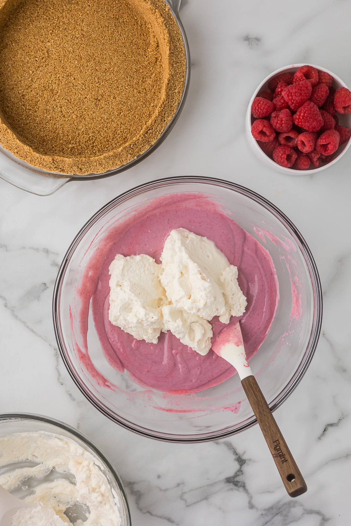 Homemade whipped cream being folded into raspberry filling for No-Bake Raspberry Lemonade Pie.