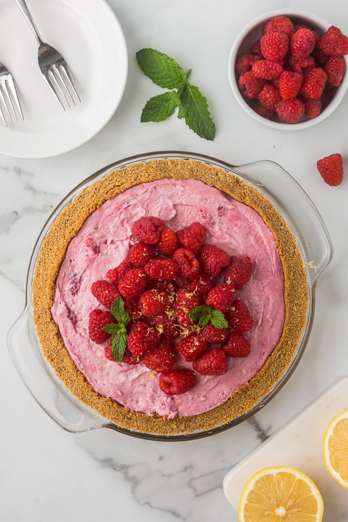 Ingredients for No-Bake Raspberry Lemonade Pie including graham crackers, raspberries, sweetened condensed milk, heavy cream, butter, lemon, sugar, and vanilla.