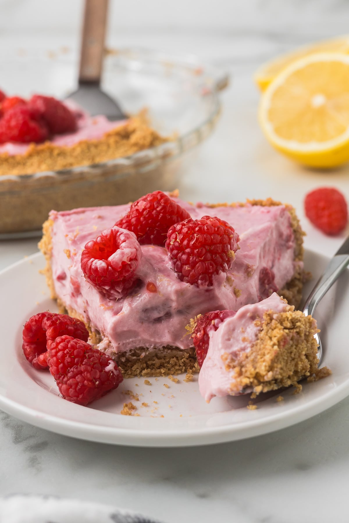 Creamy No-Bake Raspberry Lemonade Pie with fresh raspberries and a graham cracker crust on a dessert plate.