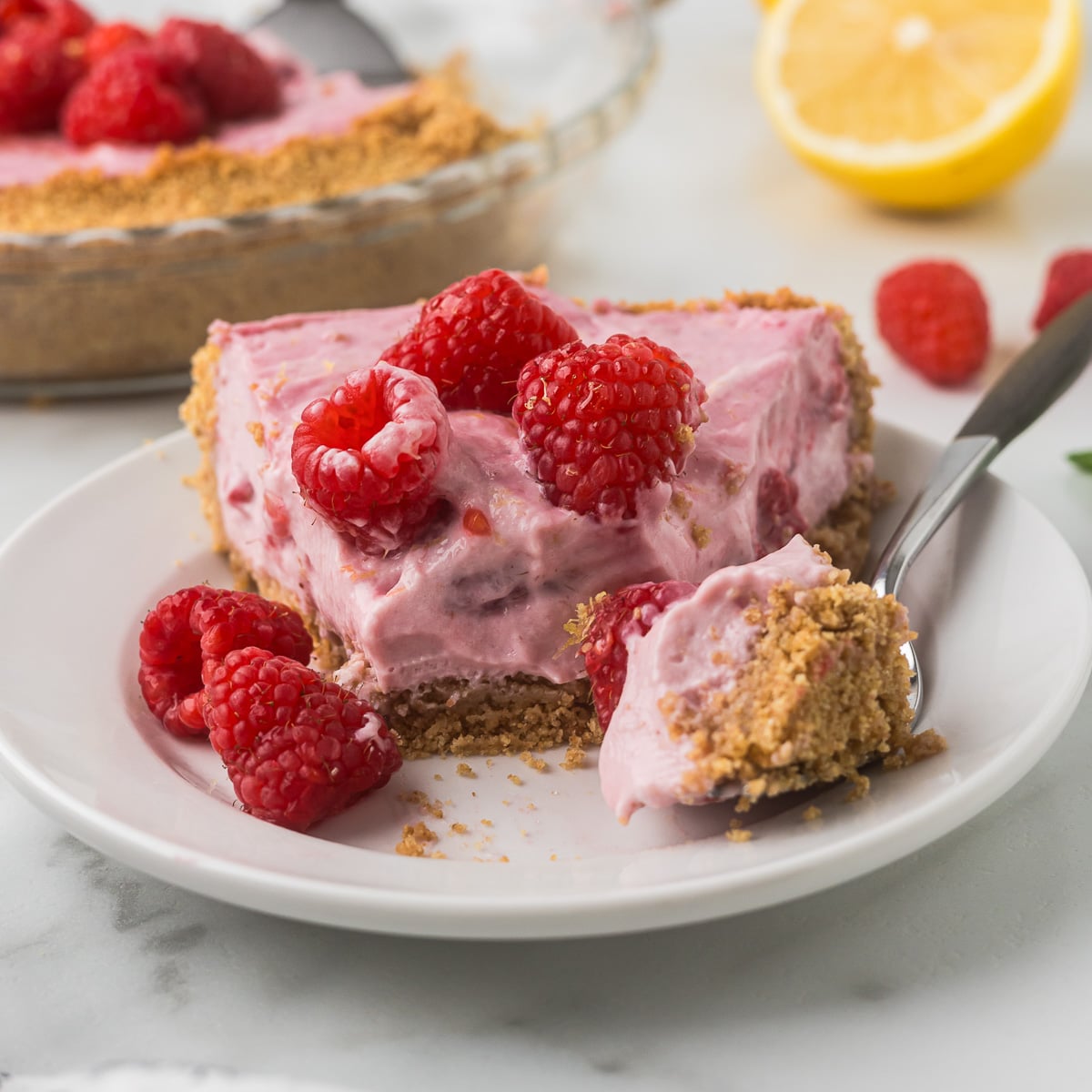 Creamy No-Bake Raspberry Lemonade Pie with fresh raspberries and a graham cracker crust on a dessert plate.